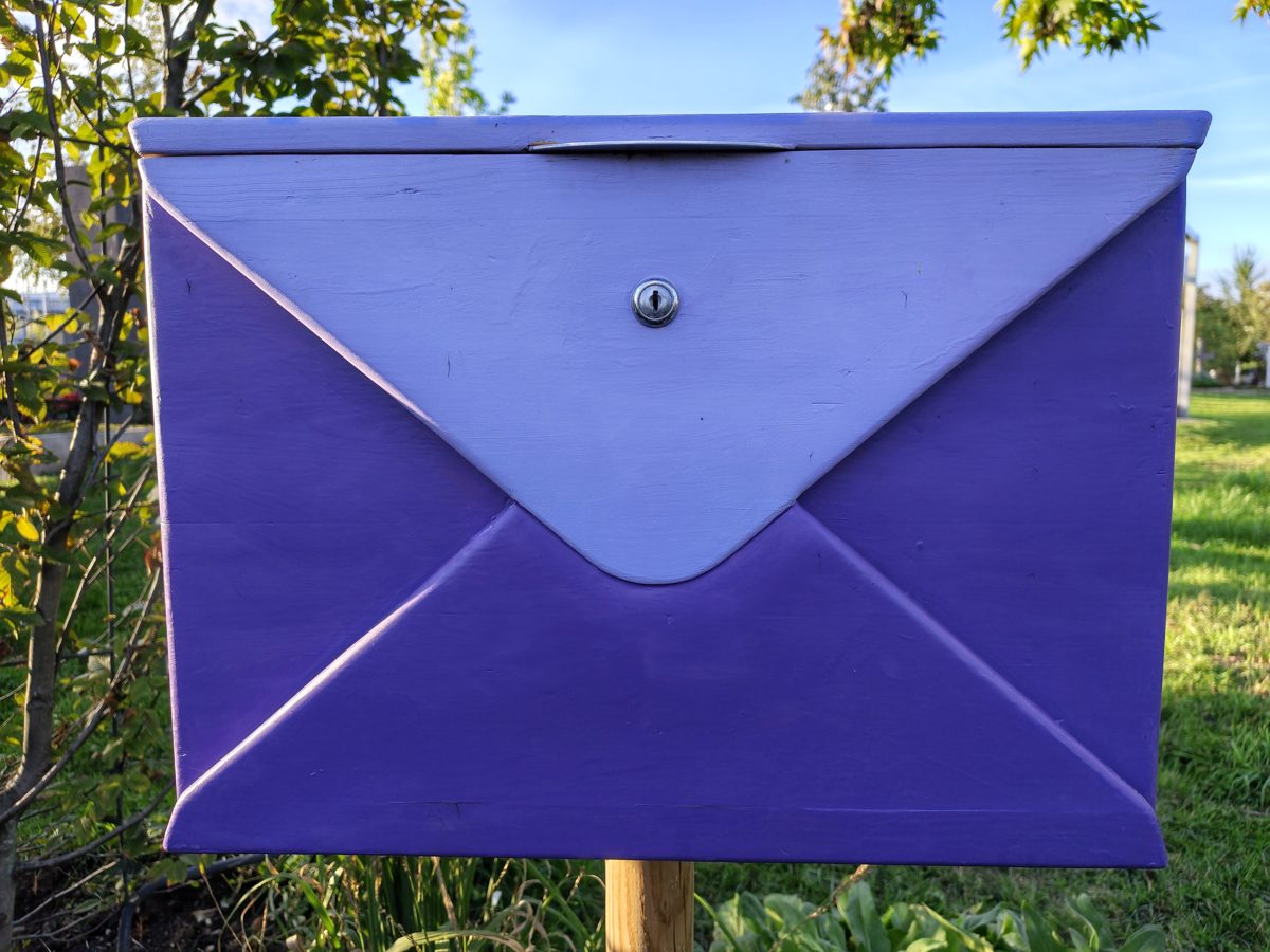 Lila Briefkasten in Briefform im Garten